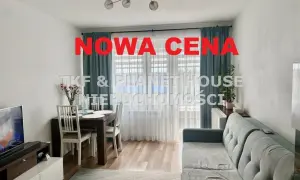 Nowa cena nieruchomości! Salon z jadalnią, kanapą i stołem. Okna z zasłonami.