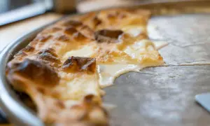 En bit av en gyllene focaccia di Recco med smält ost som rinner ut på en plåt.