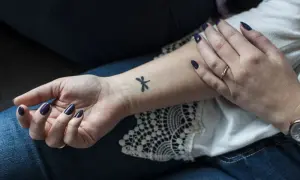 Delikatne, czarne tatuaze male na nadgarstku, w tym ważka. Dłoń ozdobiona ciemnym lakierem i pierścionkiem.