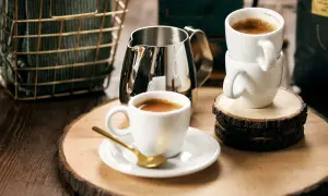 Två koppar espresso, en med en guldig sked, och en mjölkkanna på ett träfat. Perfekt för en stunds njutning med espresso bryggkaffe.