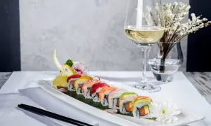 En elegant uppsättning sushirullar med färgglada toppingar, serverade med en glas vin till sushi. En vacker dukning med blommor och ätpinnar.