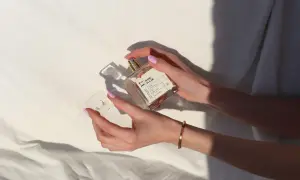 Elegancki perfum w kształcie szpilki, trzymany w dłoni z pastelowymi paznokciami. Idealny dodatek do każdej stylizacji.