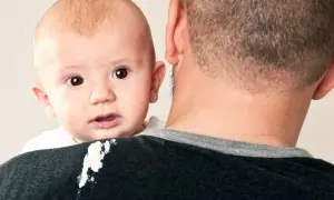 En bebis med stora ögon tittar fram över pappans axel, som har fått en kladdig fläck.