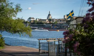Ein perfekter Blick auf Stockholm für Ihr 4 Tage Stockholm Programm: Die Skyline mit Kirche, die schwedische Flagge und ein Boot auf dem Wasser.