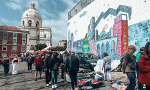 Bunter Flohmarkt in Lissabon mit Menschen, Kuppelkirche und Graffiti-Wand. Hier finden Sie echte Lissabon Geheimtipps.