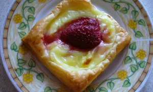 Pyszne ciasto francuskie z budyniem i truskawką na talerzu z kwiatowym wzorem.
