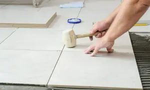 Pose de carrelage sans plinthe, un artisan ajuste une dalle avec un maillet en caoutchouc sur le mortier frais.