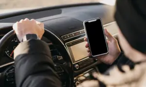 Kierowca trzyma telefon podczas jazdy, ryzykując mandat za telefon.
