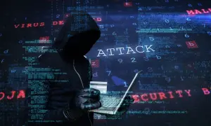 Sylwetka hakera w kapturze, trzymająca laptopa i kartę kredytową. W tle widać kod i napisy "ATTACK", "VIRUS", "MALWARE", "SECURITY", sugerujące atak hakerski.