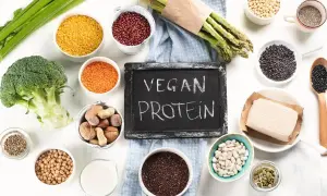 Tablica z napisem "VEGAN PROTEIN" otoczona miseczkami z roślinnymi źródłami białka: soczewicą, fasolą, orzechami, tofu, brokułem i szparagami.