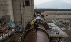 Explorateur en urbex, marchant sur un immense tuyau rouillé, traversant un grand vide industriel. Graffiti sur les murs.