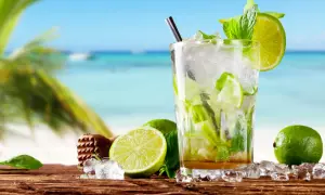 Orzeźwiający mohito czy mojito na plaży? Szklanka pełna lodu, mięty i limonki, z widokiem na turkusowe morze i palmę.