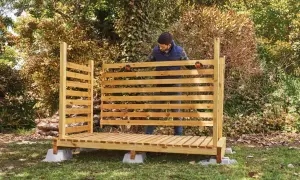 Uomo in piedi davanti a una nuova legnaia in legno, pronta per accogliere la legna per l'inverno.