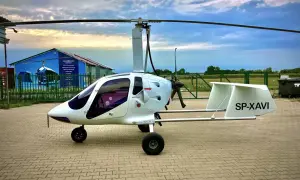 Biały wiatrakowiec SP-XAVI gotowy do lotu. Na tle chmur i niebieskiego hangaru z napisem "Loty widokowe".