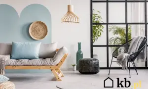 Sofa z poduszkami w kolorze baby blue, czarne krzesło z kocem, zielona butelka i rośliny w nowoczesnym wnętrzu.