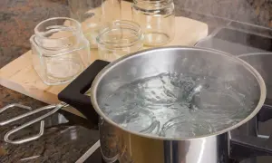 Gläser werden für das Einkochen mit Schraubdeckel sterilisiert. Ein Topf mit kochendem Wasser und ein Glasheber liegen bereit.