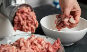 Ręka wkłada mięso do maszynki, przygotowując je do mielenia. Czy pies może jeść serca drobiowe? To mięso może być składnikiem jego diety.