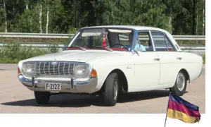 Vit Ford Taunus, en klassisk modell av svenska bilar, parkerad utomhus med en tysk flagga i förgrunden.
