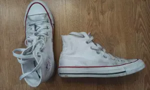 Białe trampki na drewnianym tle. Pokazują, jak wiązać trampki, z luźno zwisającymi sznurówkami.