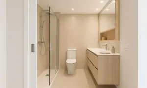 Un elegante cuarto de baño moderno con ducha de cristal, inodoro y mueble de lavabo de madera clara.
