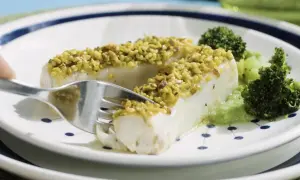 Filetti di merluzzo surgelati, impanati con pistacchi croccanti, serviti con broccoli e una salsa verde.