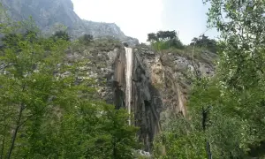 Cascata del Sopino, un velo d'acqua scende da una parete rocciosa circondata da vegetazione lussureggiante.