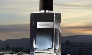 Elegancka butelka YSL EDP na tle zachodzącego słońca nad miastem.