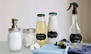 Bouteilles étiquetées "Savon Noir", "Lessive" et "Multi-usage", ainsi qu'un distributeur de savon, des pastilles et des huiles essentielles. Des produits faits maison pour un nettoyage écologique.