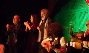 Artistas flamencos, incluyendo cantaores flamencos famosos, aplauden y tocan la guitarra en un escenario con una puerta verde de fondo.