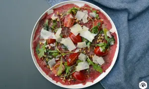 Carpaccio de bœuf finement tranché, garni de tomates cerises, roquette, pignons de pin et copeaux de parmesan. Un délice visuel et gustatif.