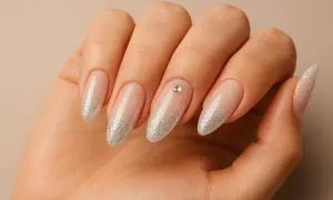 Main d'une femme aux ongles en amande, ornés d'un dégradé de paillettes argentées et d'un petit strass sur l'annulaire.