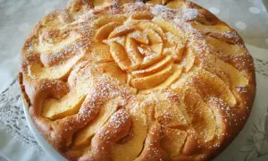 Deliziosa torta di mele senza glutine, con mele disposte a rosa al centro e spolverata di zucchero a velo.
