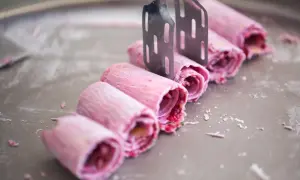 Eis selbst machen mit eismaschine: Rosa gerollte Eiscreme-Rollen werden mit zwei Spateln auf einer kalten Platte geformt.