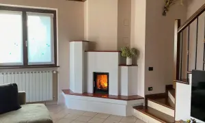 Camino moderno con fiamme vive. La struttura in **calce resiste alle alte temperature**, creando un angolo accogliente con scala e divano.
