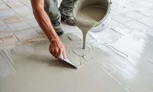 Application de béton ciré sur un carrelage existant. Un ouvrier étale le produit avec une spatule, transformant le sol.