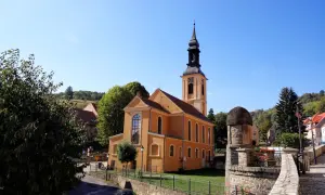Pomarańczowy kościół z wieżą zegarową na rynku. W tle zielone wzgórza, przypominające srebrną górę.