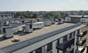 Widok na płaski dach z systemem wentylacyjnym i żwirem. Widoczne są warstwy stropodachu, elementy wentylacyjne i fragmenty budynków mieszkalnych.