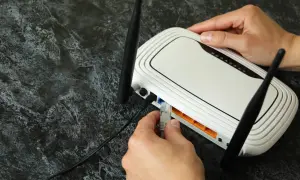 Ręka podłącza kabel sieciowy do routera, rozpoczynając konfigurację sieci domowej.