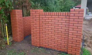 Nowy, solidny ogrodzenie z czerwonej cegły z czarnymi fugami, w trakcie budowy.