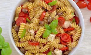 Un piatto invitante di pasta fredda con pomodorini, olive, cubetti di mozzarella e basilico fresco. Perfetta per un'estate gustosa.