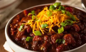 Gęste, aromatyczne chili con carne w białej misce, posypane startym serem i szczypiorkiem. Idealne na chłodne wieczory.