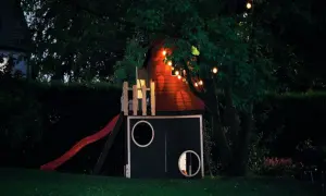 Drewniany domek ze zjeżdżalnią i światełkami, idealny do letnich zabaw dla dzieci w ogrodzie.