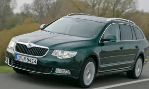 Zielone kombi auto pędzi po drodze, za nim rozmyte drzewa.