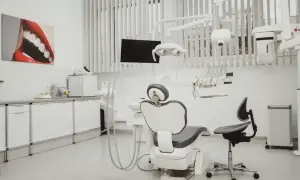 Nowoczesny gabinet stomatologiczny i ortodontyczny. Biały fotel dentystyczny, lampa, unit i szafki. Obraz z uśmiechem na ścianie.