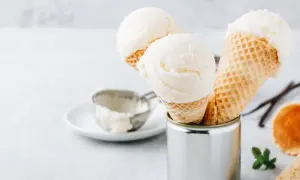 Cremiges griechischer joghurt eis ohne eismaschine in Waffelhörnchen. Ein Löffel und Vanilleschoten liegen daneben.