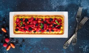 Una crostata di frutta moderna, con crema gialla e un tripudio di fragole, mirtilli e more fresche, guarnita con menta.