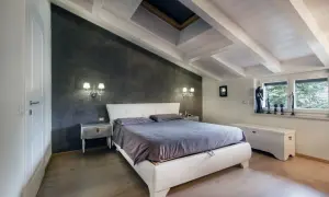 Camera da letto accogliente in un sottotetto non abitabile, con travi a vista, lucernario e pareti in resina.