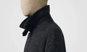 Dunkles Jackett mit hochgestelltem Kragen, der an ein Poloshirt erinnert. Das Material ist grob gewebt mit feinen roten Fäden.