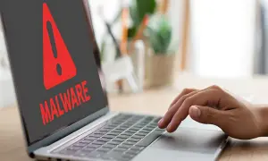 Czerwony wykrzyknik i napis "MALWARE" na ekranie laptopa, ostrzegający przed zagrożeniem, takim jak spyware.