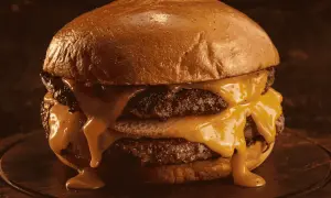 Gros plan sur un burger double au fromage fondant dégoulinant, sur un pain brioché doré.